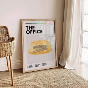 Może przedstawiać: Plakat o minimalistycznym designie z tytułem "THE OFFICE" w czarnym kolorze. Plakat przedstawia żółtą galaretkę z zszywaczem w środku. Obsada serialu jest wymieniona pod obrazkiem.