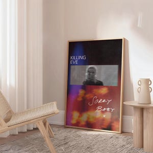 Może przedstawiać: Oprawiony plakat z napisem "KILLING EVE" w kolorze niebieskim i rozmytym zdjęciem osoby. Poniżej zdjęcia słowa "Sorry Baby" są napisane kursywą. Plakat ma złotą ramę i opiera się o ścianę.