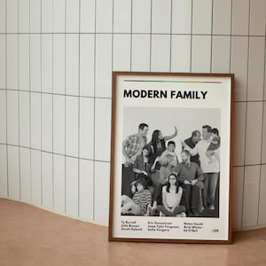 May include: A framed poster featuring the cast of "Modern Family" in a black and white group photo. The poster has a brown frame and includes the show's title and cast member names.