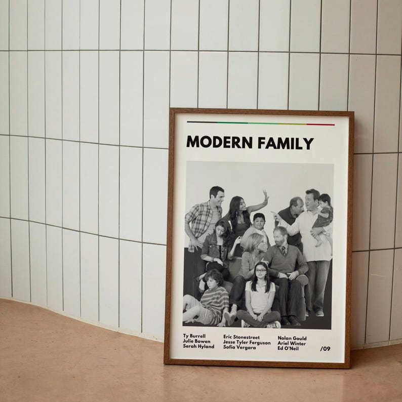 May include: A framed poster featuring the cast of "Modern Family" in a black and white group photo. The poster has a brown frame and includes the show's title and cast member names.