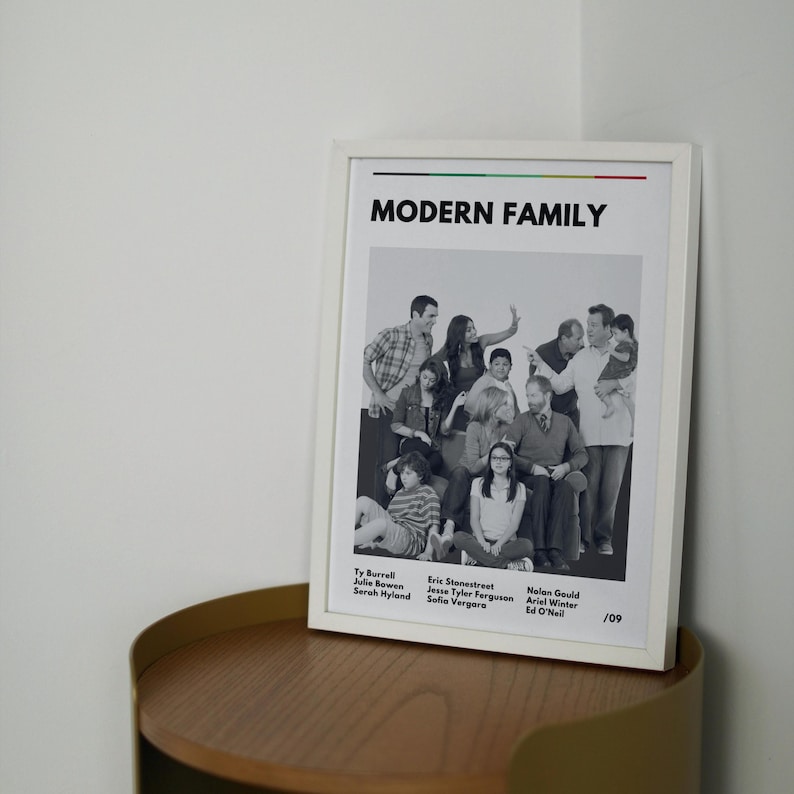 May include: A framed print featuring the cast of "Modern Family." The white frame surrounds a black and white image of the show's ensemble cast. The show's title is printed in bold black letters at the top. The names of the actors are listed at the bottom.