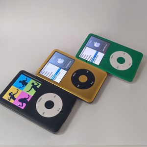Puede incluir: Tres iPods de Apple de diferentes colores. El primer iPod es negro con una silueta de una persona bailando en la pantalla. El segundo iPod es dorado con una pantalla de menú que muestra las opciones Música, Vídeos, Fotos, Extras, Podcasts, Ajustes y Reproducción aleatoria. El tercer iPod es verde con un botón de menú.