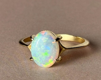 Può includere: Un anello d'oro con una pietra di opale di forma ovale. L'opale è di colore bianco latte con riflessi verdi, blu e rosa.