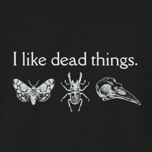 May include: Black t-shirt with white text that reads "I like dead things."  The text is centered on the shirt.  Three images are below the text: a moth, a stag beetle, and a bird skull.
