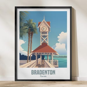 Könnte beinhalten: Gerahmter Kunstdruck mit einer stilisierten Illustration eines Uhrturms auf einem Pier in Bradenton, Florida. Das Kunstwerk hat eine Vintage-Reiseplakat-Ästhetik, mit blauem Himmel, Palmen und dem Text "BRADENTON Florida".