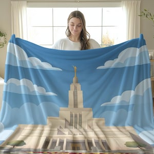 May include: A blue and white blanket featuring a detailed illustration of a temple with a gold statue on top. The design includes a blue sky with white clouds. The blanket is held up by a person.