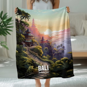 Könnte beinhalten: Eine weiche Decke mit einer Illustration der balinesischen Landschaft. Das Design zeigt Tempel, tropische Vegetation und einen Sonnenuntergang. Der Text "BALI Indonesia" ist unten auf der Decke aufgedruckt.