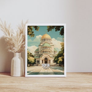 Puede incluir: Un cuadro enmarcado con una ilustración estilizada de la Catedral de Alejandro Nevski en Sofía, Bulgaria. La obra muestra la cúpula dorada y los tejados verdes de la catedral, enmarcada por árboles y un cielo azul. La palabra "SOFIA" está impresa en la parte inferior.