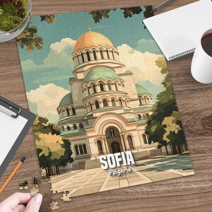 May include: A completed puzzle featuring a detailed illustration of the Alexander Nevsky Cathedral in Sofia, Bulgaria. The puzzle shows the cathedral with its gold dome and green domes, set against a blue sky with clouds. The word "SOFIA" is displayed.