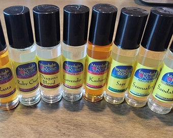 May include: Ten small glass bottles with black roll-on tops and yellow labels. Each bottle contains a different perfume oil. The labels have the text "Moonlight Rose Perfume Oil" and the name of the scent. The scents are: Easy Breezy, Rasta, Ruby Crush, Dragon's Blood, Lavender, Kashmir, Sage, Sensuality, Sandalwood, Patchouli Amber.