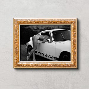K&ouml;nnte beinhalten: Schwarzwei&szlig;foto einer Frau, die sich in ein wei&szlig;es Oldtimer-Auto lehnt. Das Auto hat eine schwarze Innenausstattung und eine schwarze Sto&szlig;stange. Die Frau tr&auml;gt ein wei&szlig;es Bikini-Oberteil und einen wei&szlig;en Rock. Das Auto steht auf einem Feldweg.