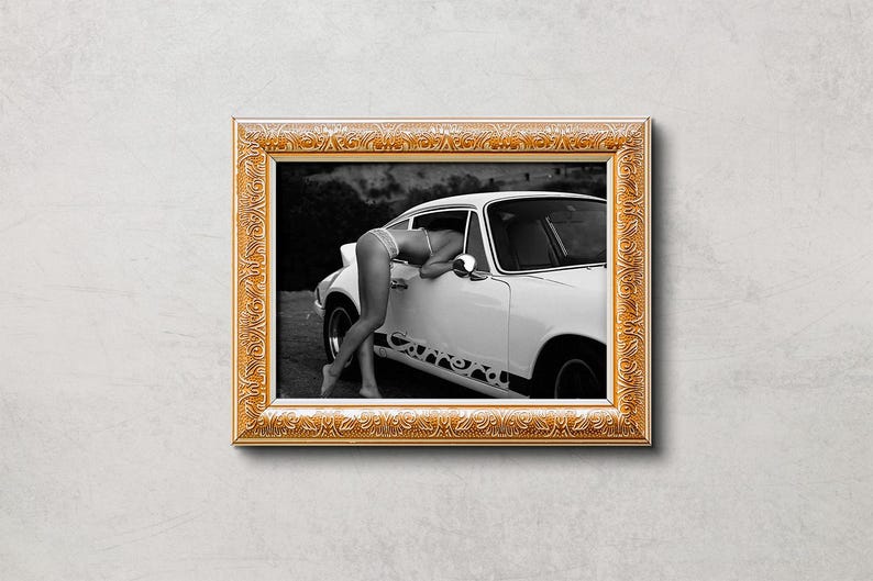 K&ouml;nnte beinhalten: Schwarzwei&szlig;foto einer Frau, die sich in ein wei&szlig;es Oldtimer-Auto lehnt. Das Auto hat eine schwarze Innenausstattung und eine schwarze Sto&szlig;stange. Die Frau tr&auml;gt ein wei&szlig;es Bikini-Oberteil und einen wei&szlig;en Rock. Das Auto steht auf einem Feldweg.