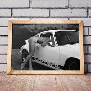 K&ouml;nnte beinhalten: Ein Schwarzwei&szlig;foto einer Frau, die sich in ein wei&szlig;es Auto mit dem Schriftzug "Carrera" an der Seite lehnt. Die Frau tr&auml;gt ein Bikini-Oberteil und Unterw&auml;sche.