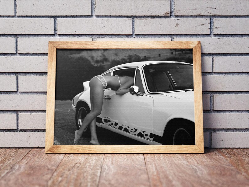 K&ouml;nnte beinhalten: Ein Schwarzwei&szlig;foto einer Frau, die sich in ein wei&szlig;es Auto mit dem Schriftzug "Carrera" an der Seite lehnt. Die Frau tr&auml;gt ein Bikini-Oberteil und Unterw&auml;sche.