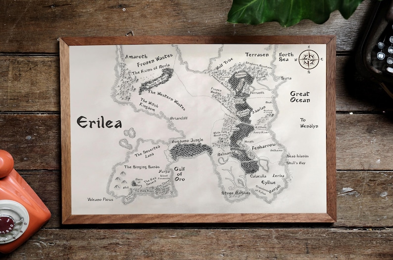 May include: A black and white hand-drawn map of the fictional land of Erilea. The map shows various regions, including the Frozen Wastes, the Western Wastes, the Gulf of Oro, and the Great Ocean. The map is framed in a brown wooden frame.