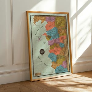 May include: A framed map print with a vintage aesthetic. The map features a colorful, stylized depiction of a coastal region, with various landmasses in shades of brown, orange, pink, and blue. The frame is a warm, light brown color. The map includes a compass rose.