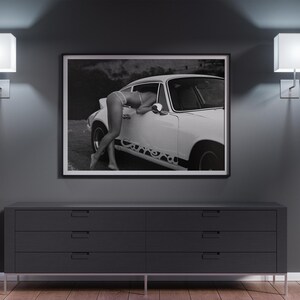 K&ouml;nnte beinhalten: Schwarzwei&szlig;foto einer Frau, die sich an ein wei&szlig;es klassisches Auto lehnt. Das Auto hat einen schwarzen Streifen an der Seite mit dem Wort "Carrera" darauf.