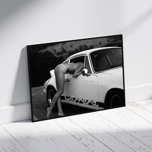 K&ouml;nnte beinhalten: Ein Schwarzwei&szlig;foto einer Frau in einem wei&szlig;en Bikini-Oberteil, die sich in ein wei&szlig;es Oldtimer-Auto lehnt. Das Auto hat einen schwarzen Streifen mit einem Design an der Seite.