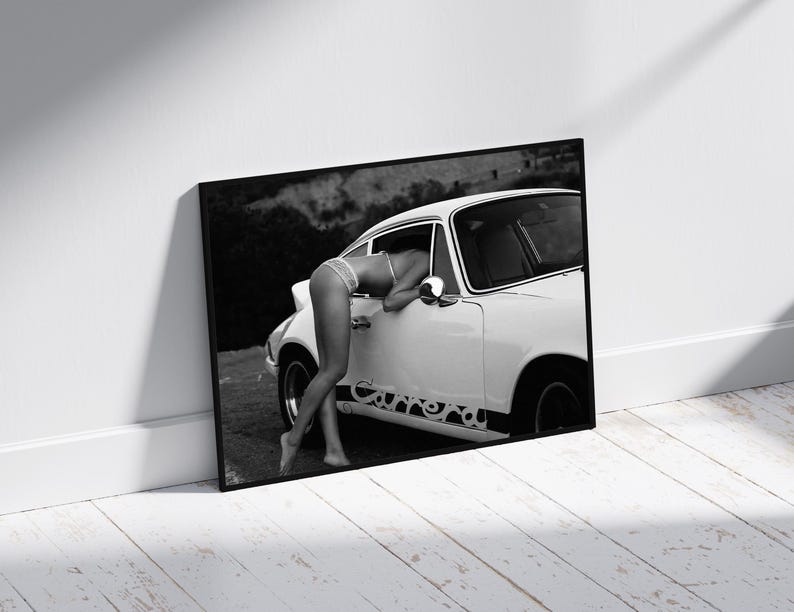 K&ouml;nnte beinhalten: Ein Schwarzwei&szlig;foto einer Frau in einem wei&szlig;en Bikini-Oberteil, die sich in ein wei&szlig;es Oldtimer-Auto lehnt. Das Auto hat einen schwarzen Streifen mit einem Design an der Seite.