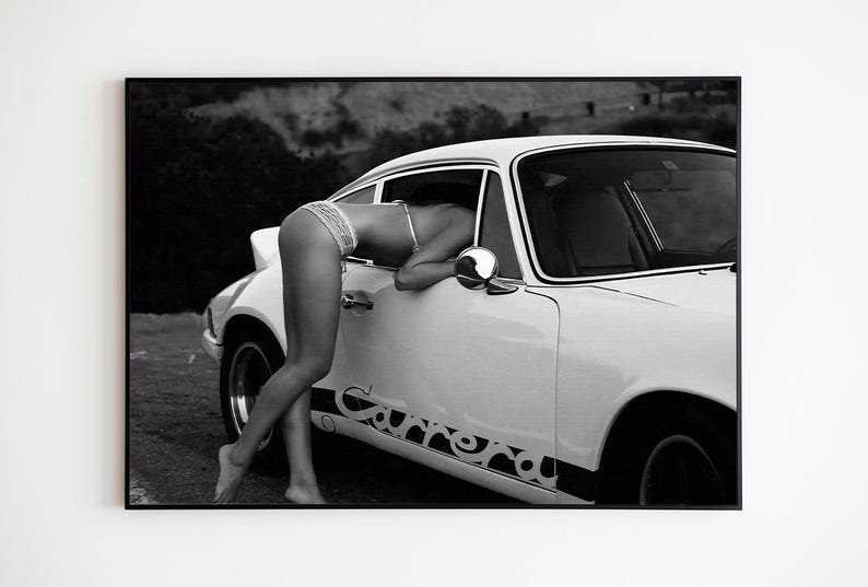 K&ouml;nnte beinhalten: Ein Schwarzwei&szlig;foto einer Frau, die sich in einen wei&szlig;en Porsche 911 Carrera lehnt. Das Auto steht auf einem Feldweg mit einem H&uuml;gel im Hintergrund.