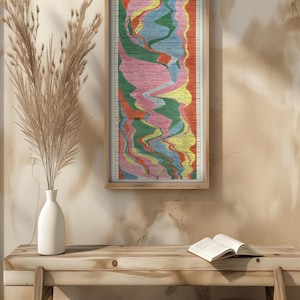 May include: A framed vintage "The Histomap" poster. The poster features a colorful, vertical timeline with various shades of red, orange, yellow, green, blue, and pink. The frame is made of light-colored wood. The poster is hanging on a beige wall.