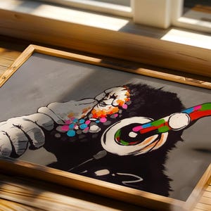 May include: A framed rectangular print featuring a stylized black and white illustration of a gorilla wearing large headphones. The gorilla's face and the headphones are accented with vibrant, multi-colored circular paint splatters and strokes.