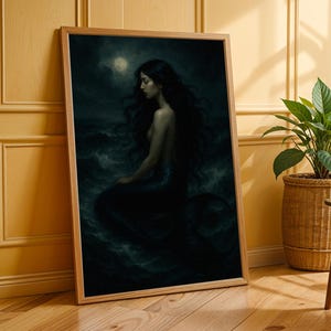 May include: A framed art print featuring a dark, moody illustration of a mermaid. The mermaid has long, flowing black hair and is seated in the ocean under a moonlit sky. The artwork is in a wooden frame, leaning against a yellow wall.