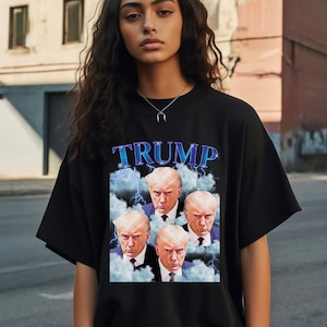 May include: Black t-shirt with a graphic print of four faces of Donald Trump in a cloud-like background with lightning bolts. The text "TRUMP" is printed in blue above the faces.