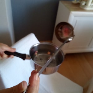 Op de afbeelding: Een roestvrijstalen thee-infuser met een lange handgreep, die wordt gebruikt om losse thee te roeren in een zilveren pan.