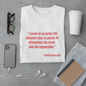 Könnte beinhalten: Weißes T-Shirt mit einem Zitat von Friedrich Nietzsche: "Ich kenne keinen besseren Lebenszweck, als im Versuch, das Große und das Unmögliche zu erreichen, zu sterben."