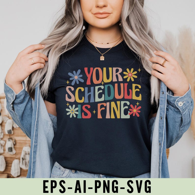 Pu&ograve; includere: T-shirt blu navy con la scritta "YOUR SCHEDULE IS FINE" in lettere colorate in stile retr&ograve;. Il design include accenti floreali in vari colori. La persona indossa anche una giacca di jeans. Il testo "EPS-AI-PNG-SVG" &egrave; visibile.