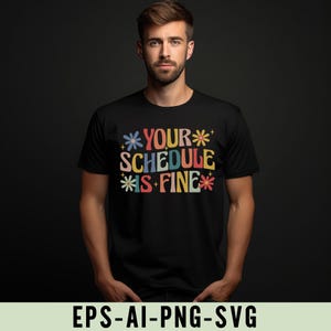 Pu&ograve; includere: T-shirt nero con la scritta "YOUR SCHEDULE IS FINE" in lettere colorate in stile retr&ograve;. Il design include accenti floreali. La maglietta &egrave; girocollo e viene indossata da una persona.