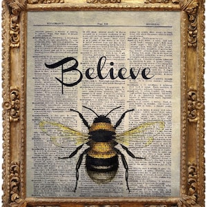May include: A framed print featuring a vintage dictionary page with the word "Believe" in elegant script. A detailed illustration of a bumblebee is centered below the text. The frame is ornate with a gold finish.