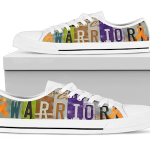 Puede incluir: Zapatillas de lona blancas con la palabra "WARRIOR" en letras coloridas. El diseño incluye una cinta naranja. Los zapatos se presentan en una caja blanca.