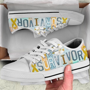 Puede incluir: Zapatillas de lona blancas con la palabra "SURVIVOR" impresa en los laterales con un diseño de matrícula. Los zapatos presentan una cinta amarilla y cordones blancos. Las zapatillas están en una caja.