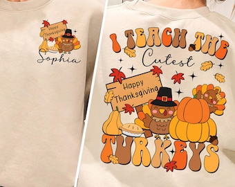 May include: A beige sweatshirt with a Thanksgiving-themed design. The front of the sweatshirt has a small turkey and the text "Happy Thanksgiving" and "Sophia". The back of the sweatshirt has a larger turkey with a pumpkin and the text "I Teach The Cutest Turkeys" and "Happy Thanksgiving".