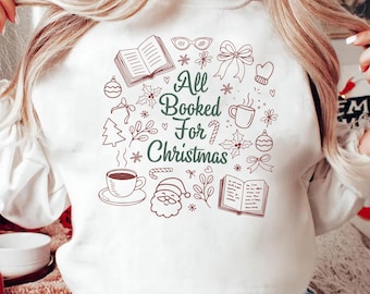 May include: White sweatshirt with a festive design. The design includes the text "All Booked For Christmas" surrounded by illustrations of books, coffee cups, ornaments, and other holiday-themed elements. A cozy and seasonal apparel item.