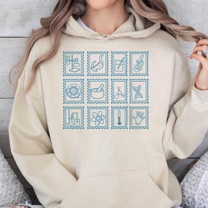 Pu&ograve; includere: Felpa con cappuccio beige con un design di francobolli blu con illustrazioni a tema scientifico. I francobolli includono immagini di beute, un microscopio e un filamento di DNA. La felpa ha un cappuccio con coulisse e una tasca a marsupio.