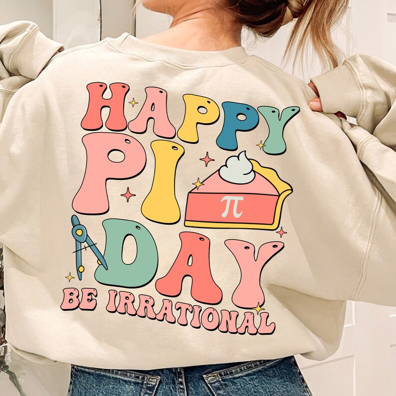 May include: A beige sweatshirt with a colorful graphic print that says "Happy Pi Day Be Irrational". The graphic includes a pie with a whipped cream topping and the symbol for pi.