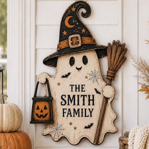 May include: A decorative wooden wall hanging shaped like a ghost wearing a black witch hat with a crescent moon and stars. The ghost holds a jack-o'-lantern lantern and a broom, featuring the text THE SMITH FAMILY, spiderwebs, and bats.