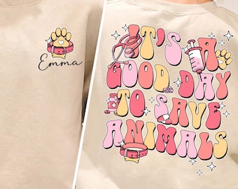 May include: A beige sweatshirt with a pink paw print and the word "Emma" on the front. The back of the sweatshirt has a pink, yellow, and white graphic that says "It's a good day to save animals".