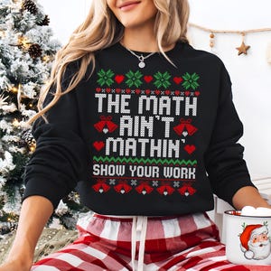 May include: Black Christmas sweater with a red and green knit pattern. The sweater has the text "The Math Ain't Mathin' Show Your Work" on it.