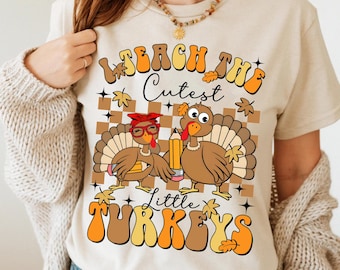 May include: A beige t-shirt with a graphic of two turkeys. The text on the shirt reads "Teach the Cutest Little Turkeys".