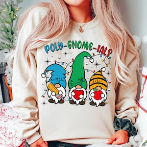 May include: A beige sweatshirt with the text "POLY-GNOME-IALS" in green, blue, and yellow letters. Three gnomes are depicted wearing hats and holding a pencil, a heart, and an apple. Each gnome has a math equation on their hat.