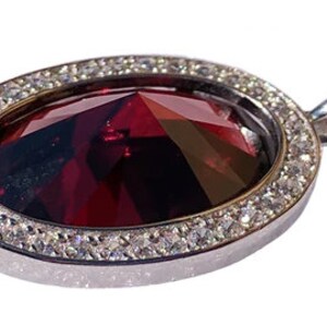 May include: A silver pendant with a large, oval-shaped, red gemstone surrounded by a halo of smaller, clear gemstones.