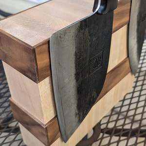 May include: Two black chef's knives with wooden handles are mounted on a wooden magnetic knife holder. The holder is made of light and dark wood and has a layered design.
