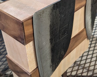 May include: Two black chef's knives with wooden handles are mounted on a wooden magnetic knife holder. The holder is made of light and dark wood and has a layered design.