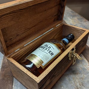 May include: A wooden box with a brass latch, open to reveal a bottle of Old Forester Kentucky Straight Bourbon Whiskey.