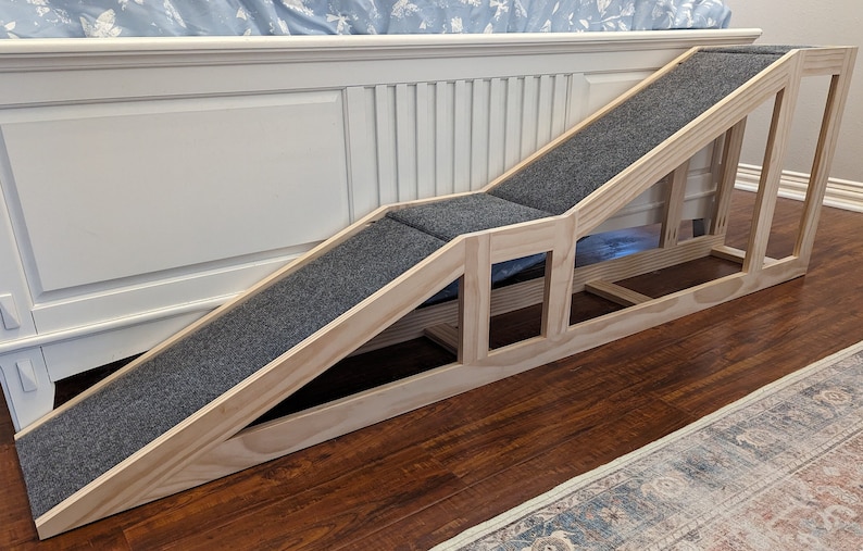 May include: A wooden pet ramp with a gray carpet surface. The ramp is designed to help pets get on and off a bed or couch. The ramp is made of sturdy wood and has a non-slip surface.