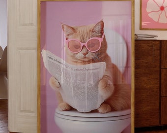 Könnte beinhalten: Ein gerahmter Druck eines Katers, der eine rosa Sonnenbrille trägt und eine Zeitung liest, während er auf einer Toilette sitzt. Der Hintergrund ist eine rosa Wand.